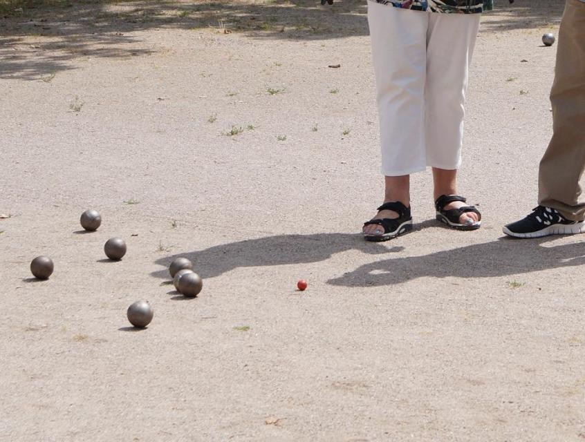 Boulekugeln auf Sand und die Beine von zwei Personen Boulekugeln auf Sand und die Beine von zwei Personen