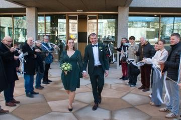 Ein frisch vermähltes Paar kommt glücklich lächelnd aus dem Bürgerhaus und läuft durch im Spalier stehende Gratulanten, die alle applaudieren und wehende Fähnchen in den Händen halten.