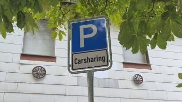 Carsharing-Schild vor Hauswand und Blättern eines Baumes