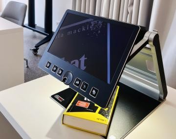Lesegerät mit Buch darunter auf einem Schreibtisch