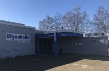 Ansicht auf den Eingangsbereich der Halle mit Schriftzug bei Sonnenschein