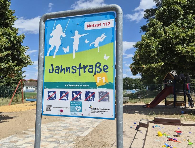 Spielplatzbild mit Schild Jahnstraße - F1, Schaukeln, Sandkasten und Rutsche
